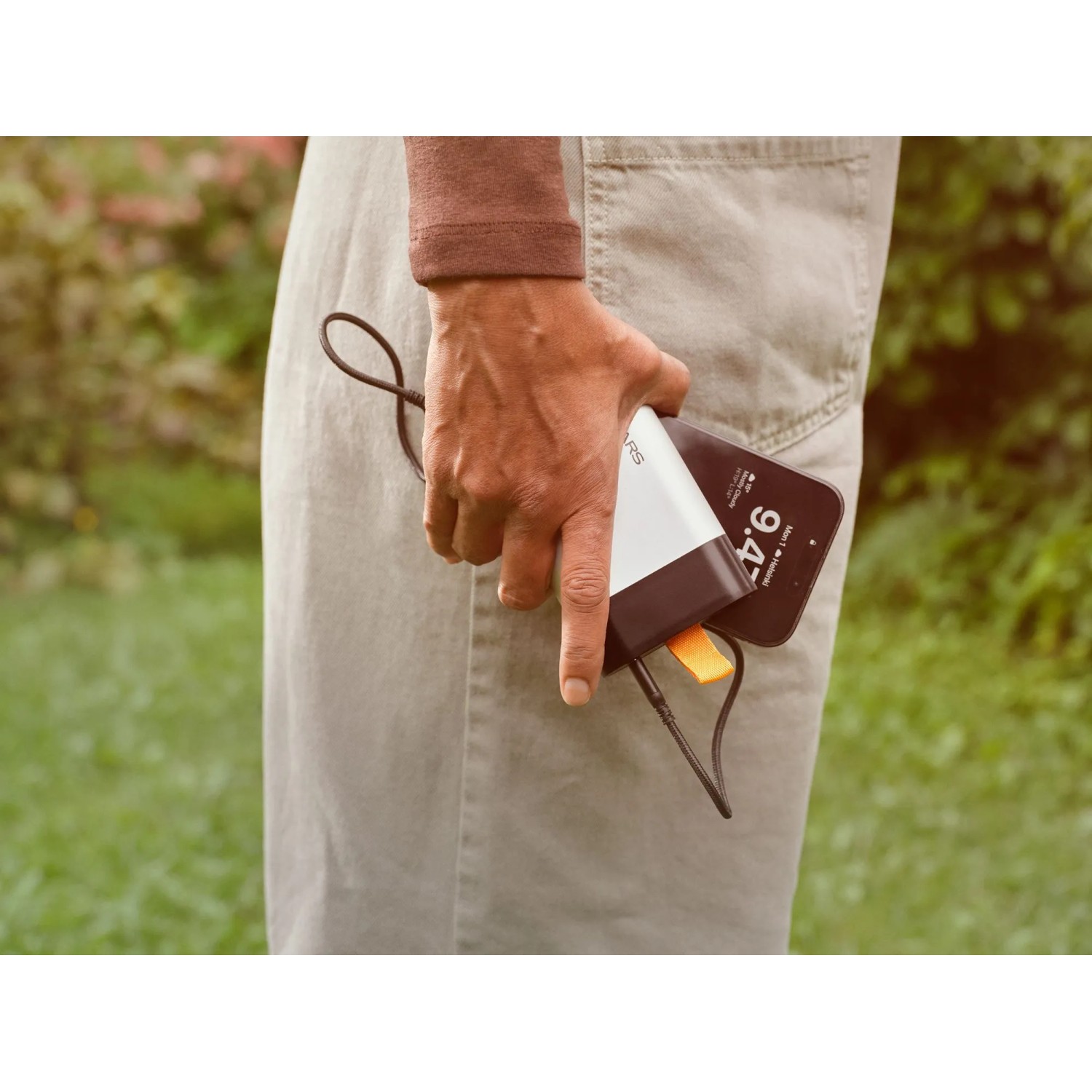 Fiskars Akku 12V 4Ah lädt Smartphone per USB-C. Weiße Powerbank in Hand, draußen.