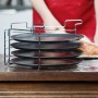 Pizzablech 4er Set mit Ständer: Vier antihaftbeschichtete, gelochte Backbleche aus Eisen im Metallgestell auf Holztisch. Für Pizza.