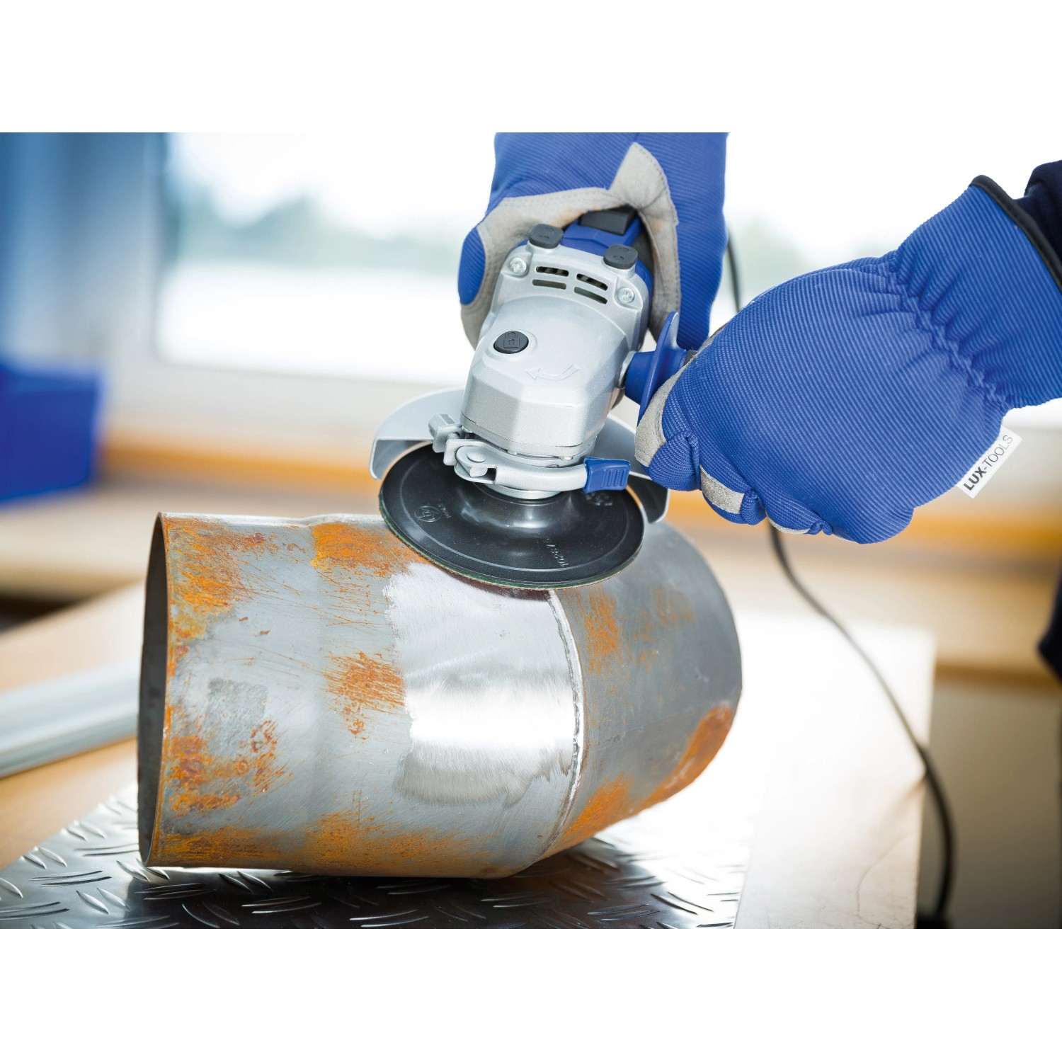 LUX Fiberscheibe Classic im Einsatz mit Winkelschleifer zum Entrosten eines Metallrohrs.
