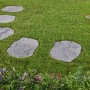 Grau-nuancierte Trittplatten Nativa in Natursteinoptik auf Rasen und zwischen Blumen im Garten.