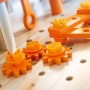 Detail der OBI Kinderwerkbank: orange Zahnräder und Schrauben auf heller Holzplatte mit Löchern.