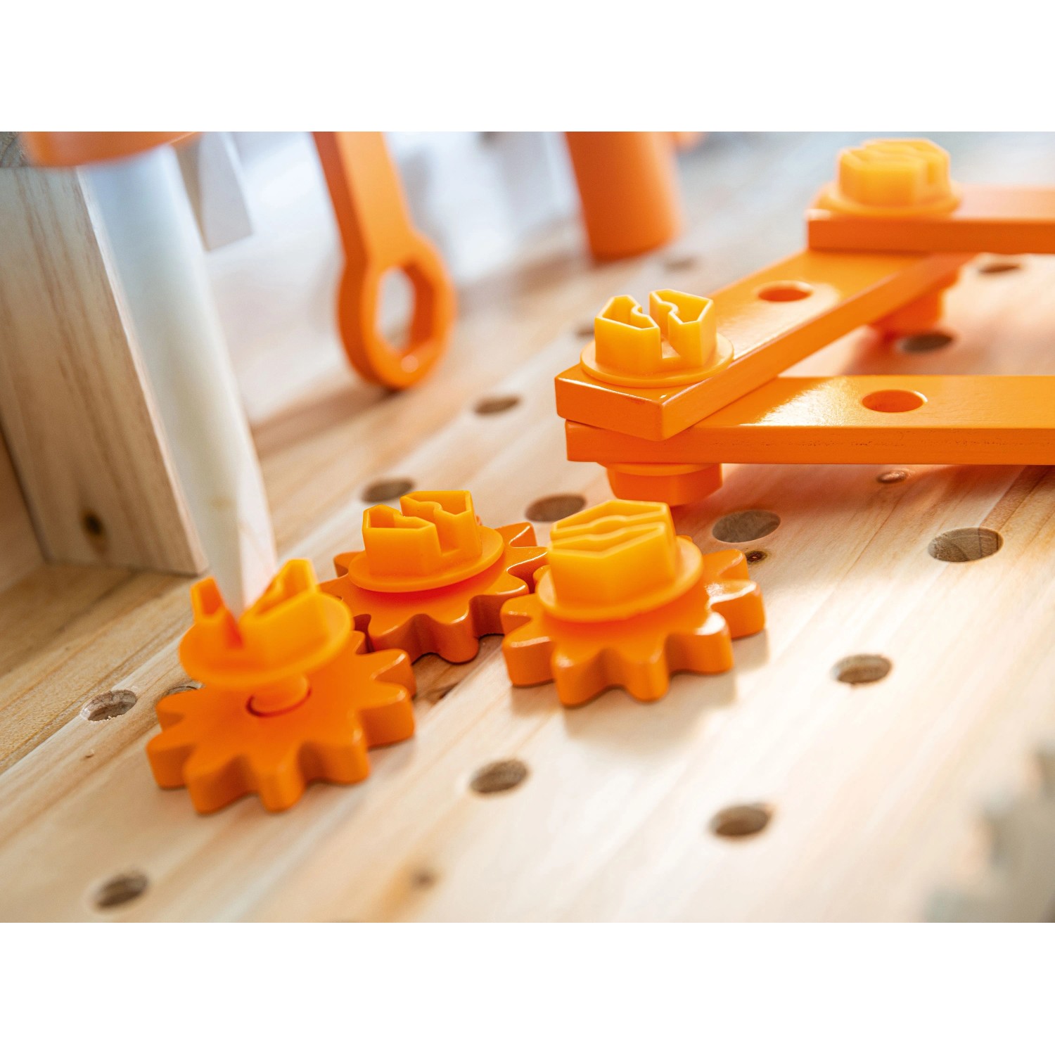 Detail der OBI Kinderwerkbank: orange Zahnräder und Schrauben auf heller Holzplatte mit Löchern.
