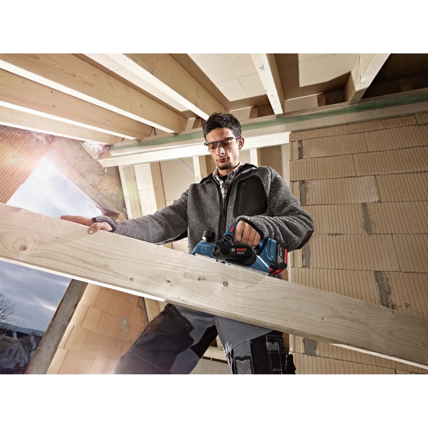 Bosch Professional Akku-Hobel GHO 18V-LI Solo im Einsatz beim Hobeln eines Holzbalkens.