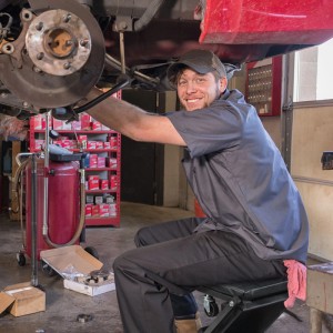 Mann sitzt auf schwarzem Relaxdays Montagerollbrett als Werkstatthocker unter einem Auto. Stahlkonstruktion, drehbare Rollen.