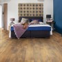 Verlegtes Living by Haro Laminat 7mm Eiche Fattoria im Schlafzimmer mit Bett und blauer Wand.