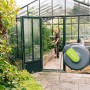 Geka Schlauchbox K25 Grau an Steinwand, Person bewässert Pflanzen im Gewächshaus.
