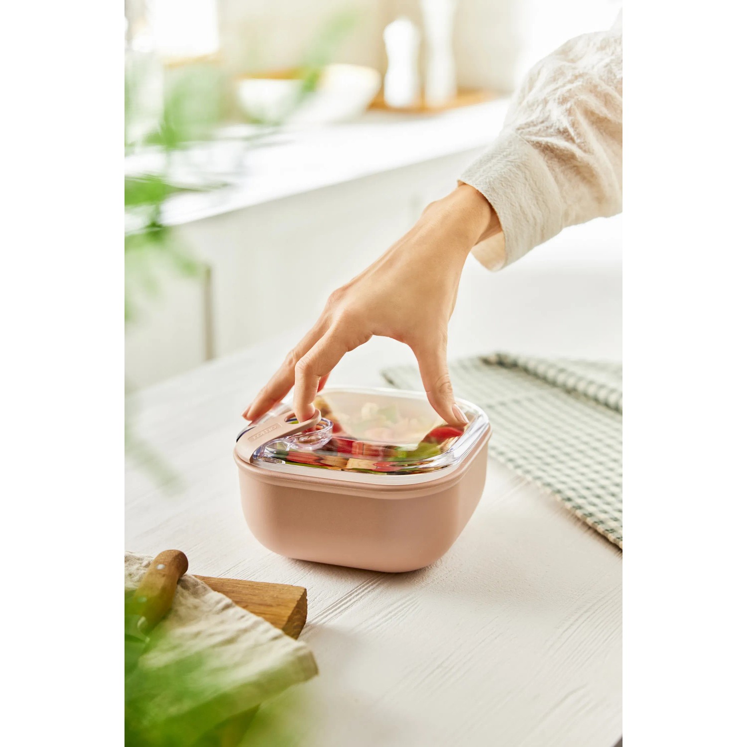 Rosa Rotho Frischhaltedose Ela 1 l mit Salat und Hand auf Tisch.