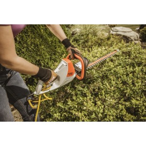 Person schneidet Hecke mit orange-grauer Stihl Elektro-Heckenschere HSE 52. Leichte Heckenschere für Gartenarbeiten.