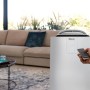 Weißes De'Longhi Klimagerät PAC-AP140i im Wohnraum mit Fernbedienung.