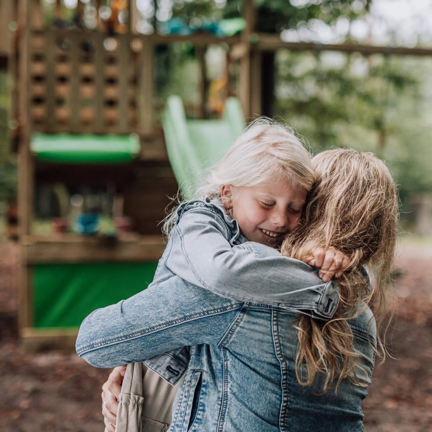 Mädchen umarmt Mutter vor Fatmoose Spielturm KiwiKey mit Rutsche (Apfelgrün).