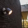 Lutec LED-Außenwandspot Explorer an dunkler Backsteinwand. Schwenkbare Außenleuchte mit warmweißem Licht.