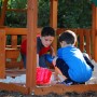 Kinder spielen im Sandkasten des Backyard Discovery Skyfort II Spielturms mit Schaukel und Rutsche.