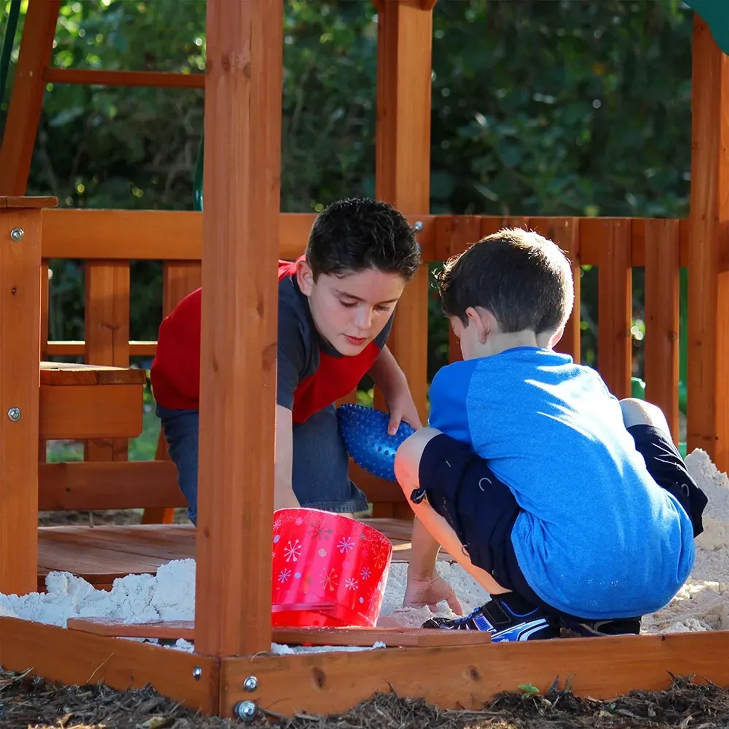 Kinder spielen im Sandkasten des Backyard Discovery Skyfort II Spielturms mit Schaukel und Rutsche.