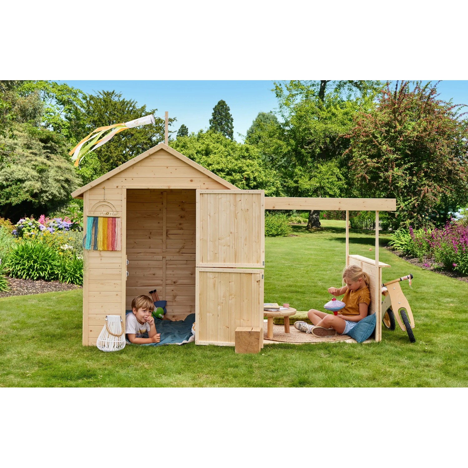 Soulet Kinderspielhaus Eugenie mit Terrasse und zwei spielenden Kindern im Garten.