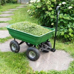 Grüner Wiltec Gartenwagen mit Kippfunktion, gefüllt mit Grasschnitt, auf einem Gartenweg.