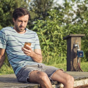 Mann bedient Gardena Bluetooth Bewässerungssteuerung per Smartphone im Garten.
