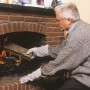 Mann legt mit LUX Arbeitshandschuhen Holz in Kamin. Lange Stulpe schützt vor Hitze.