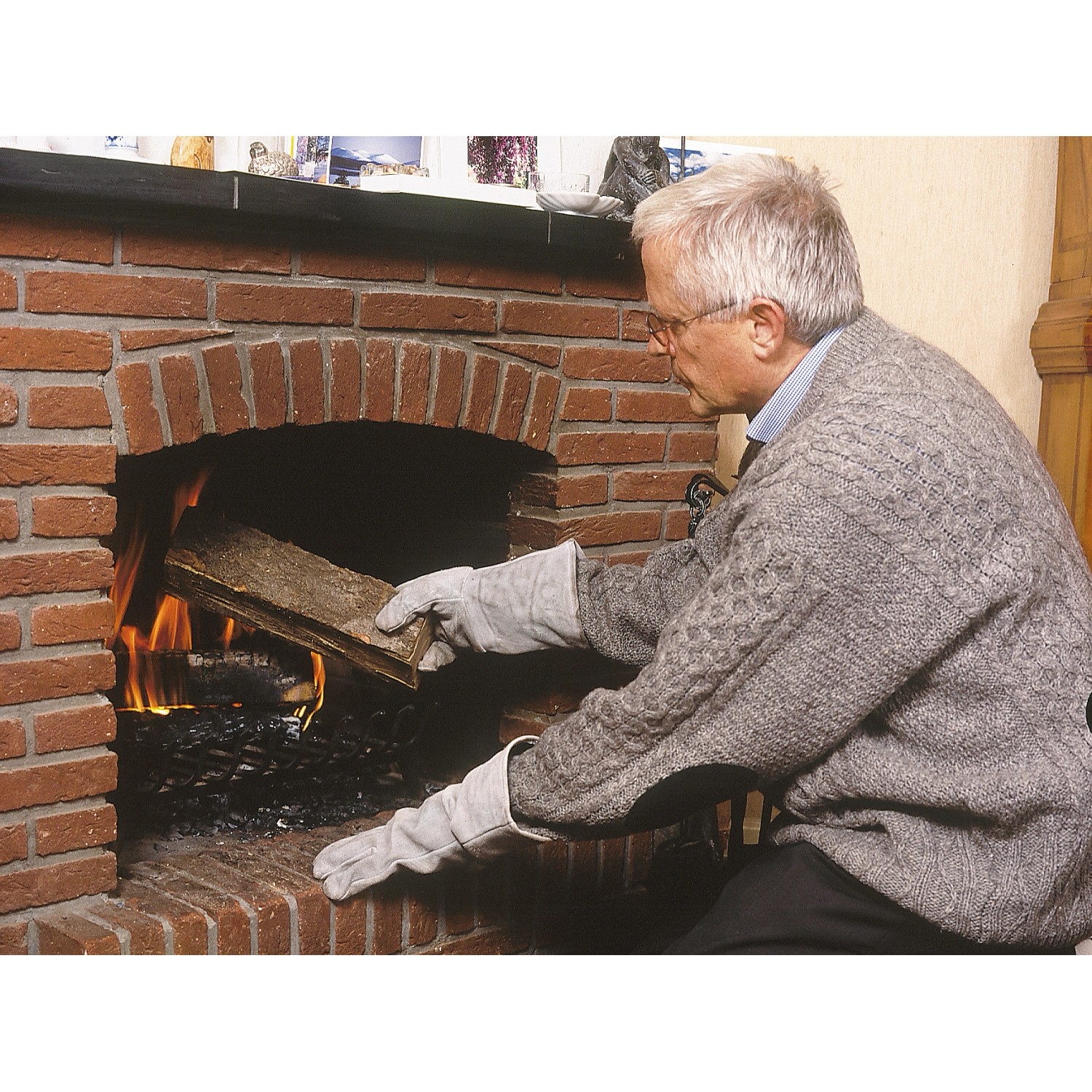 Mann legt mit LUX Arbeitshandschuhen Holz in Kamin. Lange Stulpe schützt vor Hitze.