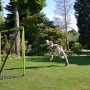 Grün-schwarzes EXIT Tempo Fußballtor (240x160cm) aus Stahl im Garten, ein Kind köpft einen Ball.