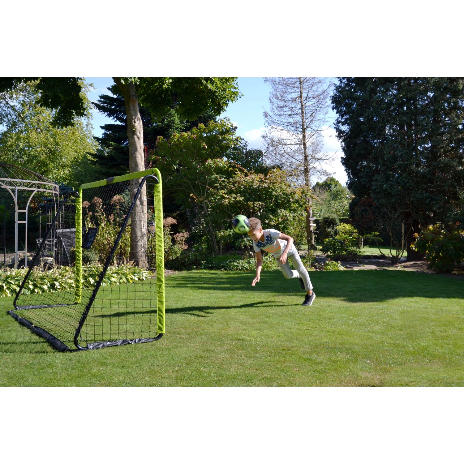 Grün-schwarzes EXIT Tempo Fußballtor (240x160cm) aus Stahl im Garten, ein Kind köpft einen Ball.