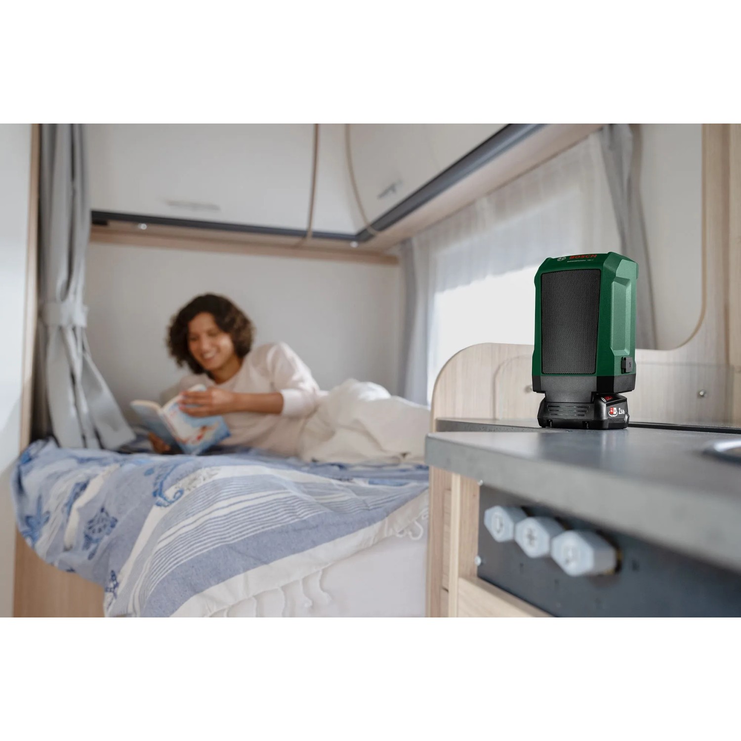 Grüner Bosch Akku-Bluetooth-Lautsprecher UniversalSpeaker 18V-1 auf Tisch in Wohnmobil. Kompaktes Akkugerät für kabelloses Streaming.
