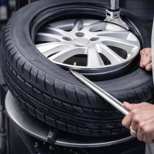 Hände montieren schwarzen Autoreifen mit silbernem Montierhebel auf Alufelge. Wiltec Reifen Montiereisen Set für Auto, Quad.