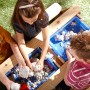 Kinder spielen am Sand- und Wasserspieltisch Nick Braun im Garten.