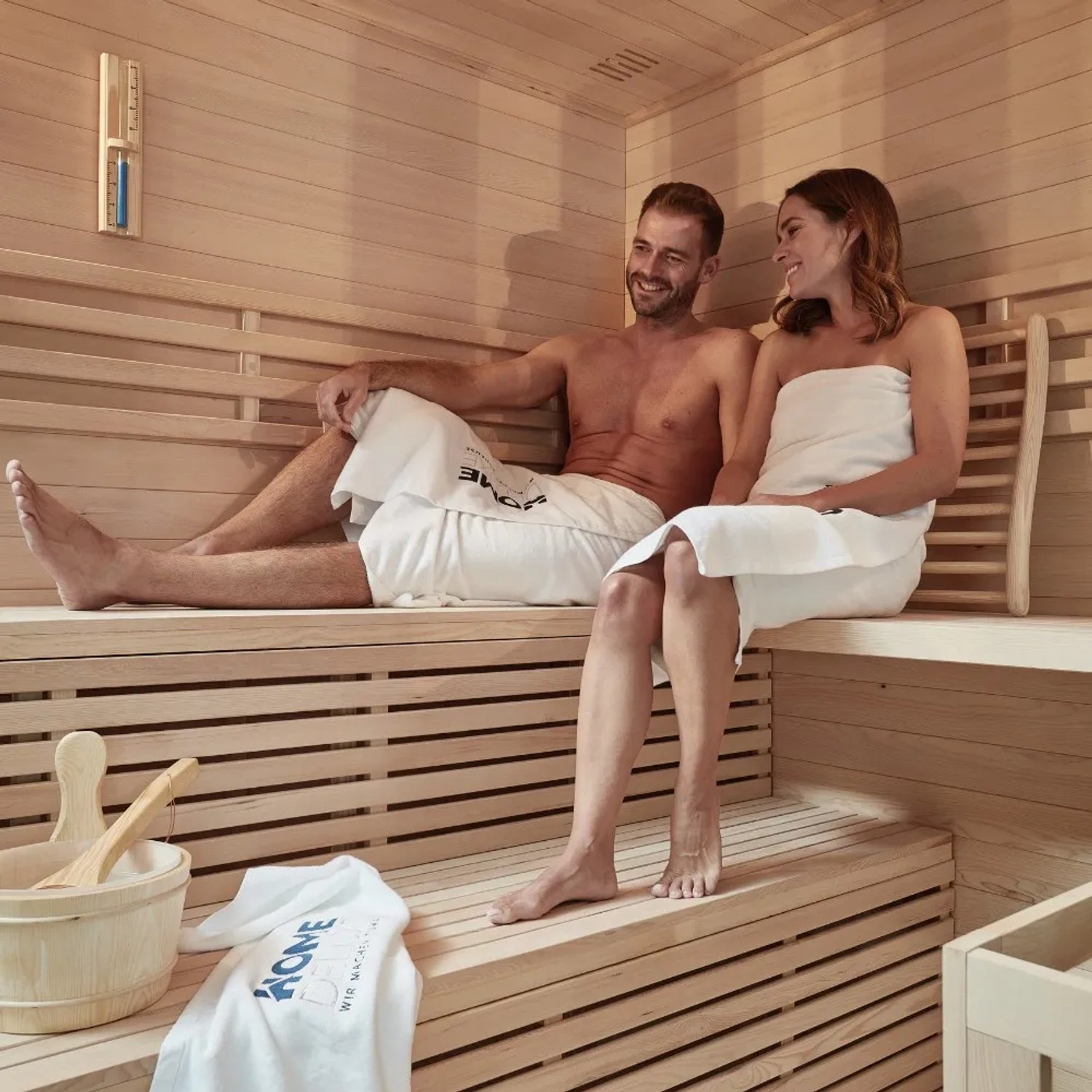 Paar entspannt in der SKYLINE BIG Sauna aus Tannenholz. Holzverkleidung und Bänke sichtbar.