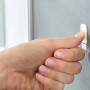 Anbringung eines Tesa Powerstrips Haken Waterproof Zoom Edelstahl Small an einer grauen Wand.