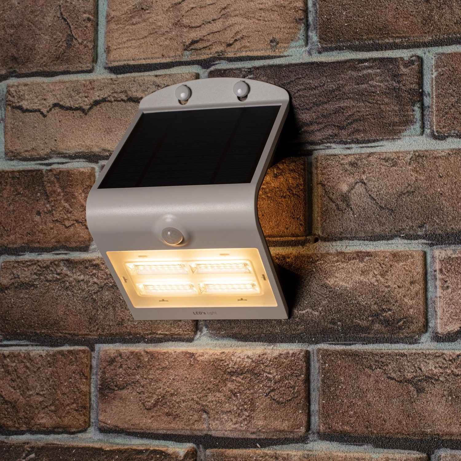 Weiße LED Solar-Außenleuchte mit Sensor, 3,2W, 400lm, 3000K, montiert an einer Backsteinwand.
