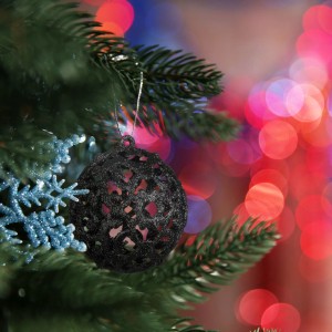 Schwarze, glitzernde Weihnachtskugel aus Kunststoff mit Lochmuster hängt am grünen Christbaum. Festliche Baumdekoration.