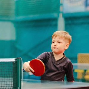 Kind spielt Tischtennis mit grünem Netz und rotem Schläger. Tischtennisnetz zum Klemmen für Sport & Familienspaß.