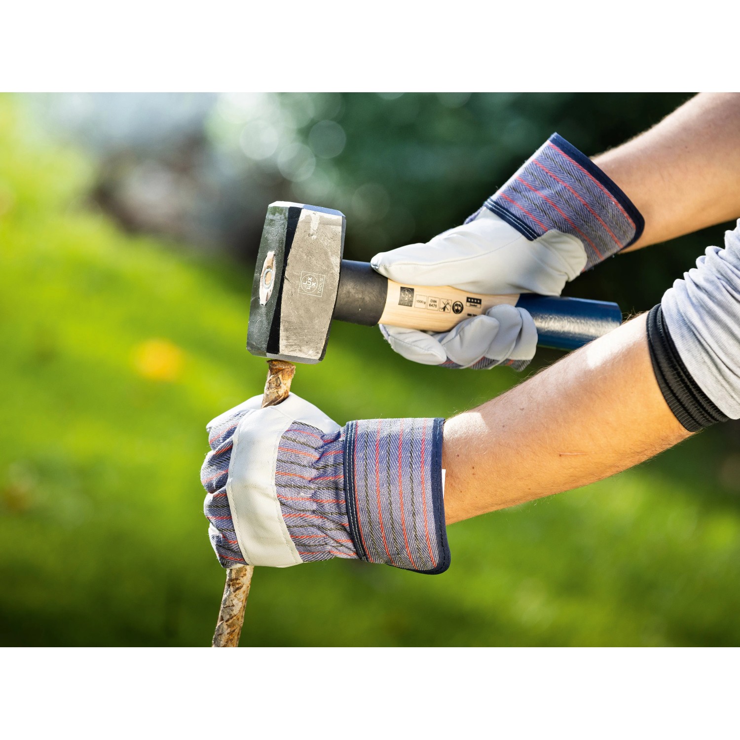Hände mit Arbeitshandschuhen Gr. 8 beim Spalten von Holz mit einem Hammer.