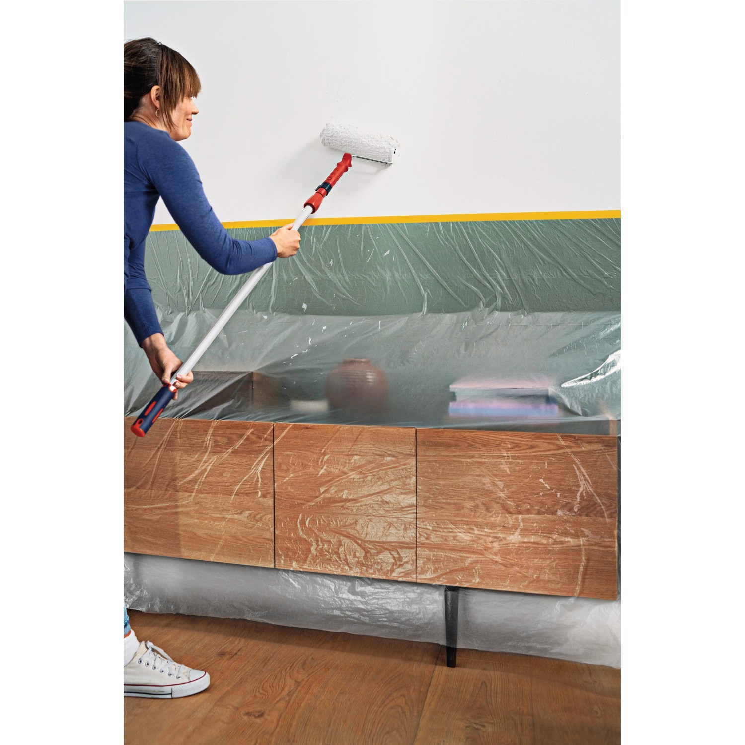 Frau streicht Wand mit Tesa Abdeckfolie Easy Cover. Möbel und Boden sind abgedeckt.
