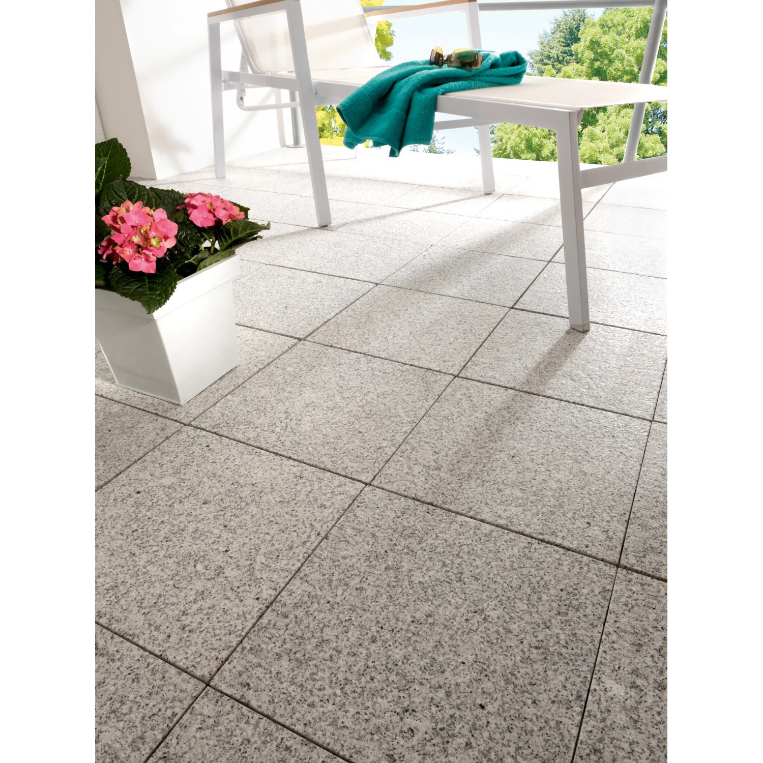 Verlegte Klickfliesen Naturstein Sino Grau, 30x30cm, auf einer Terrasse mit Gartenmöbeln und Pflanze.