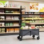 Grauer faltbarer Bollerwagen mit verstellbarem Griff und Rädern mit Bremsen, beladen mit Einkäufen, in einem Supermarkt.