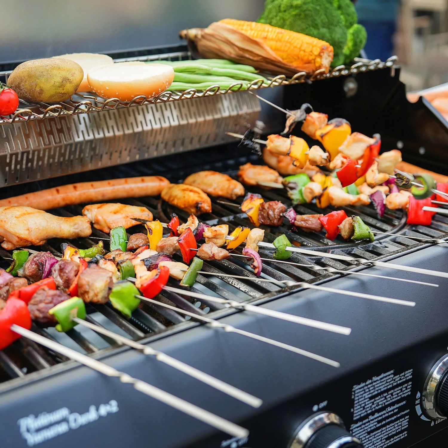 Taino Platinum Yamara Dark 4+2 Gasgrill mit Grillgut wie Spießen, Würstchen und Gemüse.