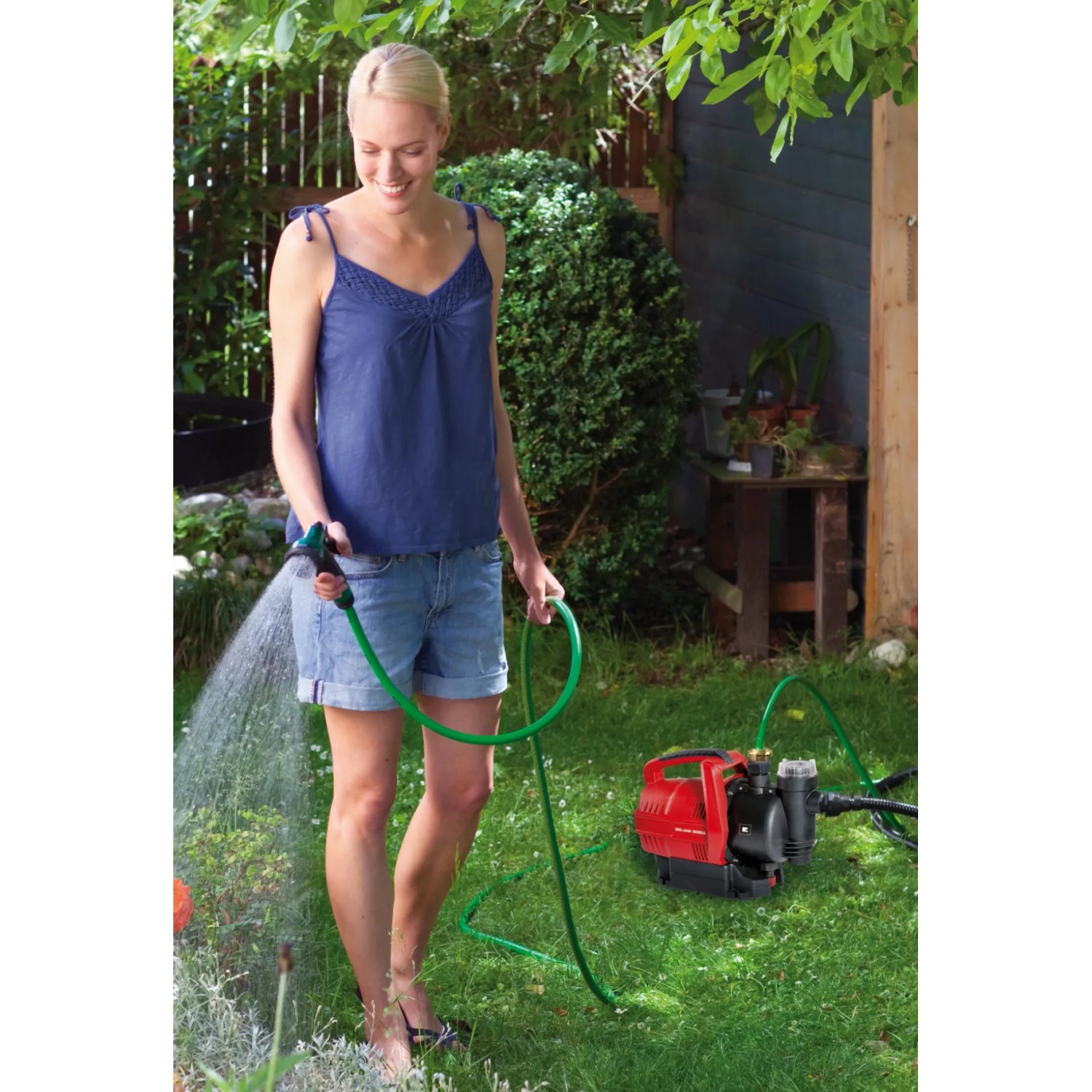 Frau bewässert Garten mit Einhell Hauswasserautomat GC-AW 6333. Elektro-Pumpe mit Schlauch.