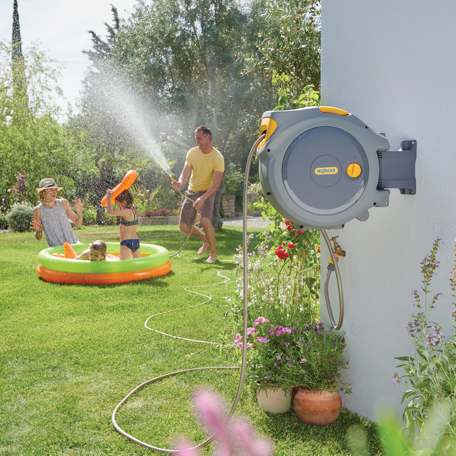 Hozelock Auto Reel Schlauchtrommel mit 30m Schlauch im Einsatz: Kinder spielen mit Wasser im Garten.