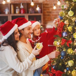 Fröhliche Familie schmückt Tannenbaum mit goldenen und bunten Weihnachtskugeln aus dem 72er Set. Festlicher Christbaumschmuck.