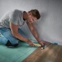 Mann verlegt Laminat mit Wolfcraft Verlege-Set: Schlagholz, Zugeisen und Keile im Einsatz.
