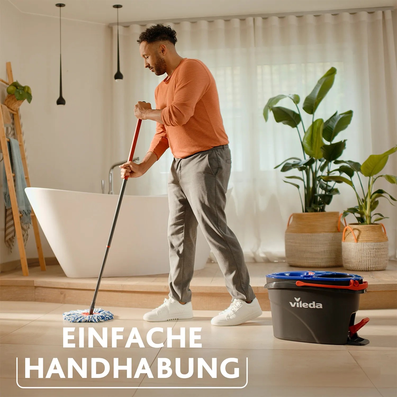 Mann wischt Boden mit Vileda H2PrO Reinigungs-Set. Eimer mit Zweitanksystem im Hintergrund.