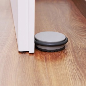 Wagner Bodentürstopper Big Disk Color steingrau vor weißer Tür auf Holzboden.