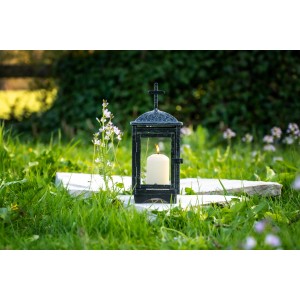 Schwarze FlowerPower Grablaterne Rubi mit brennender Kerze auf Grabstein im Grünen.