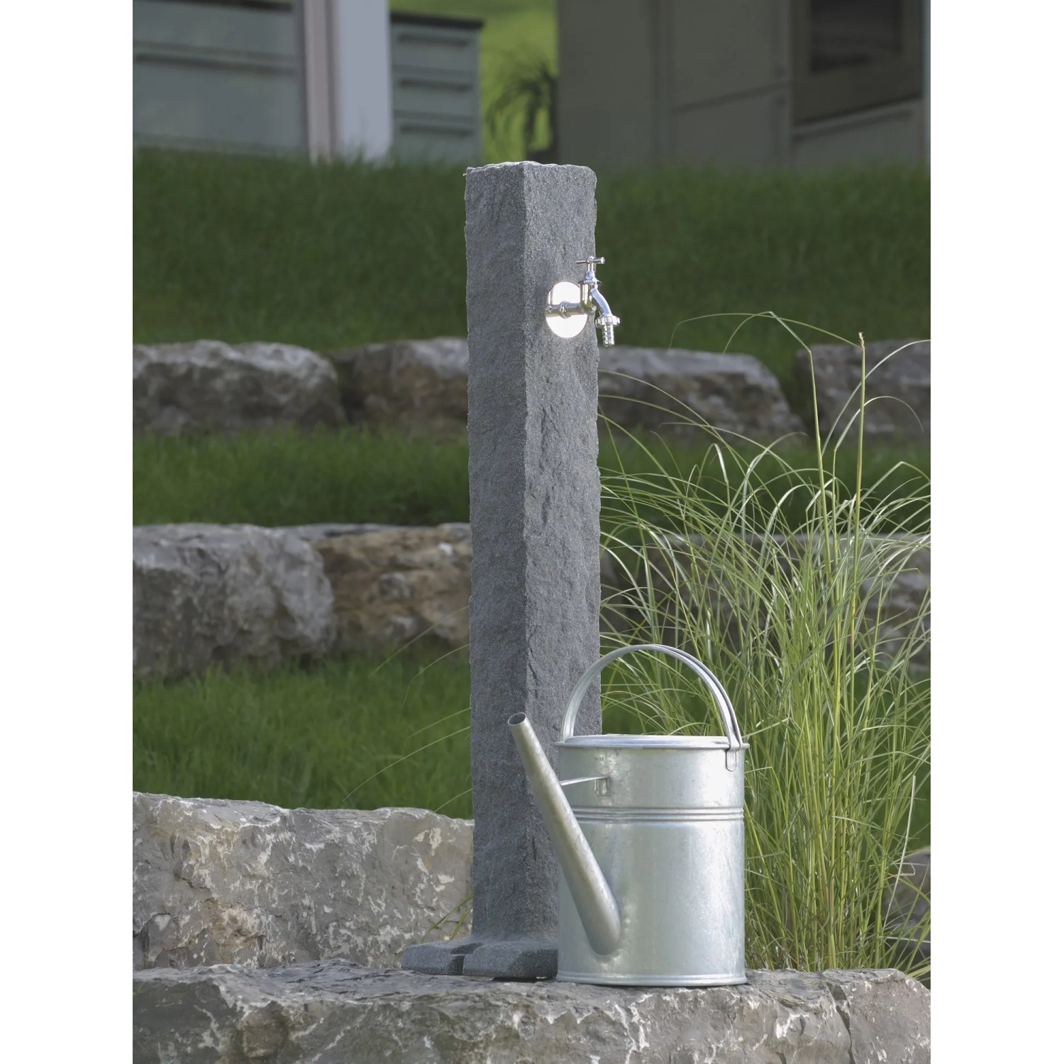 Arves Wasserzapfstelle Natura Black Granit mit Wasserhahn und Gießkanne im Garten.