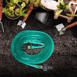 Grüner, flacher Relaxdays Bewässerungsschlauch (5 m) aus Kunststoff auf Erde, mit Gartenwerkzeug im Hintergrund.
