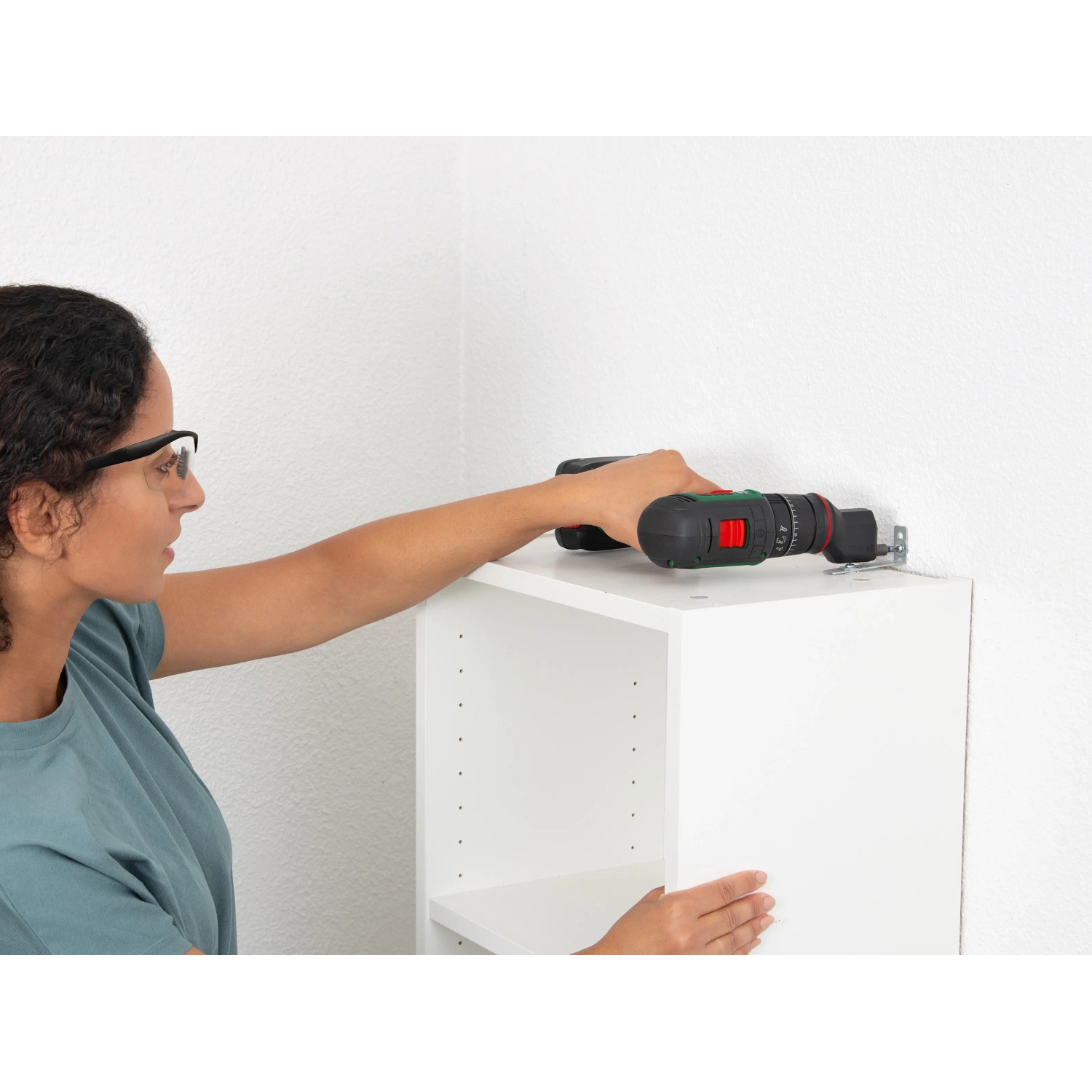 Frau schraubt mit Bosch Akku-Bohrschrauber AdvancedDrill 18V-80 Solo einen Schrank an die Wand.