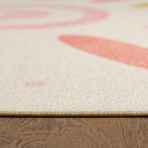 Cremefarbener Kurzflor Kinderteppich mit rosa Mustern. Detailansicht des Ayyildiz Play Teppichs auf Holz.