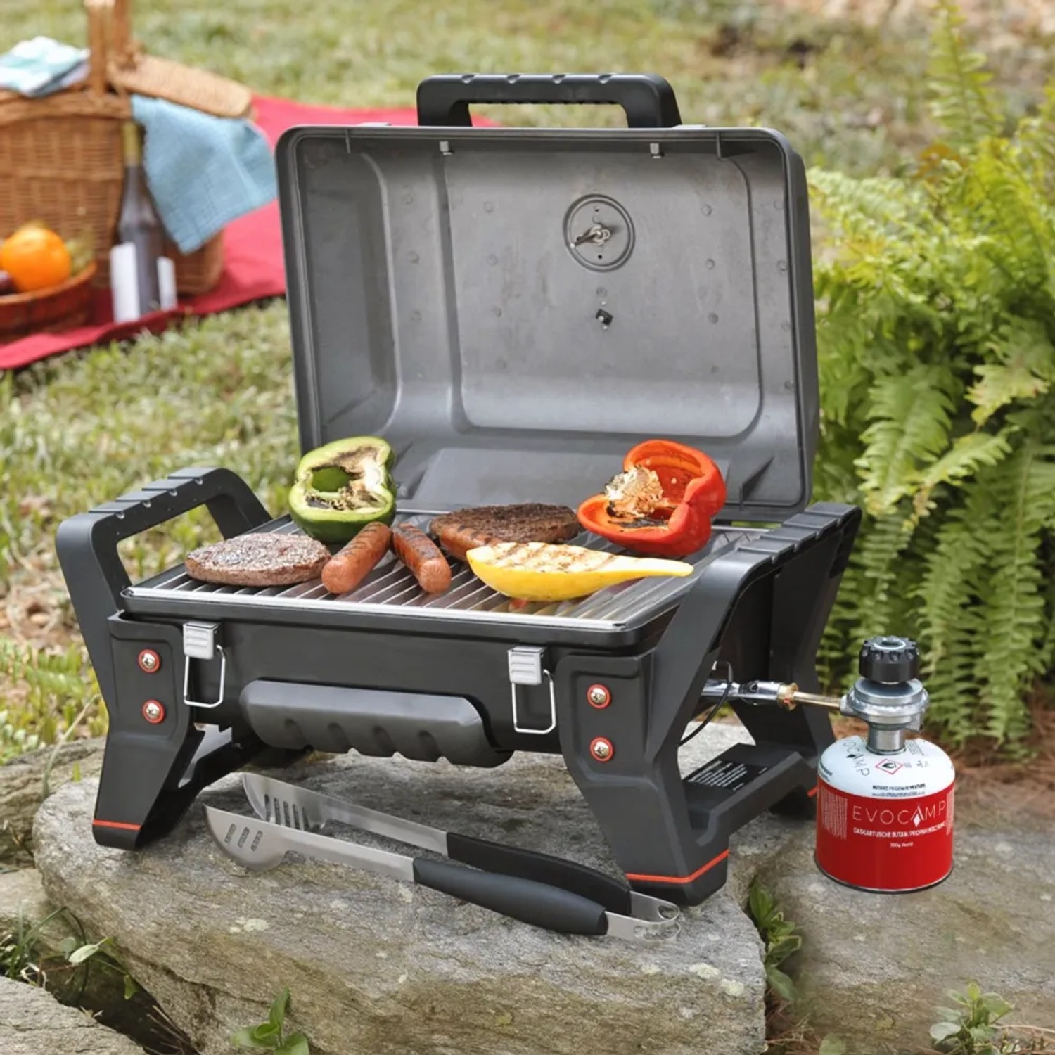 Evocamp Gasgrill mit Gaskartusche, Grillgut und Grillzange im Freien.