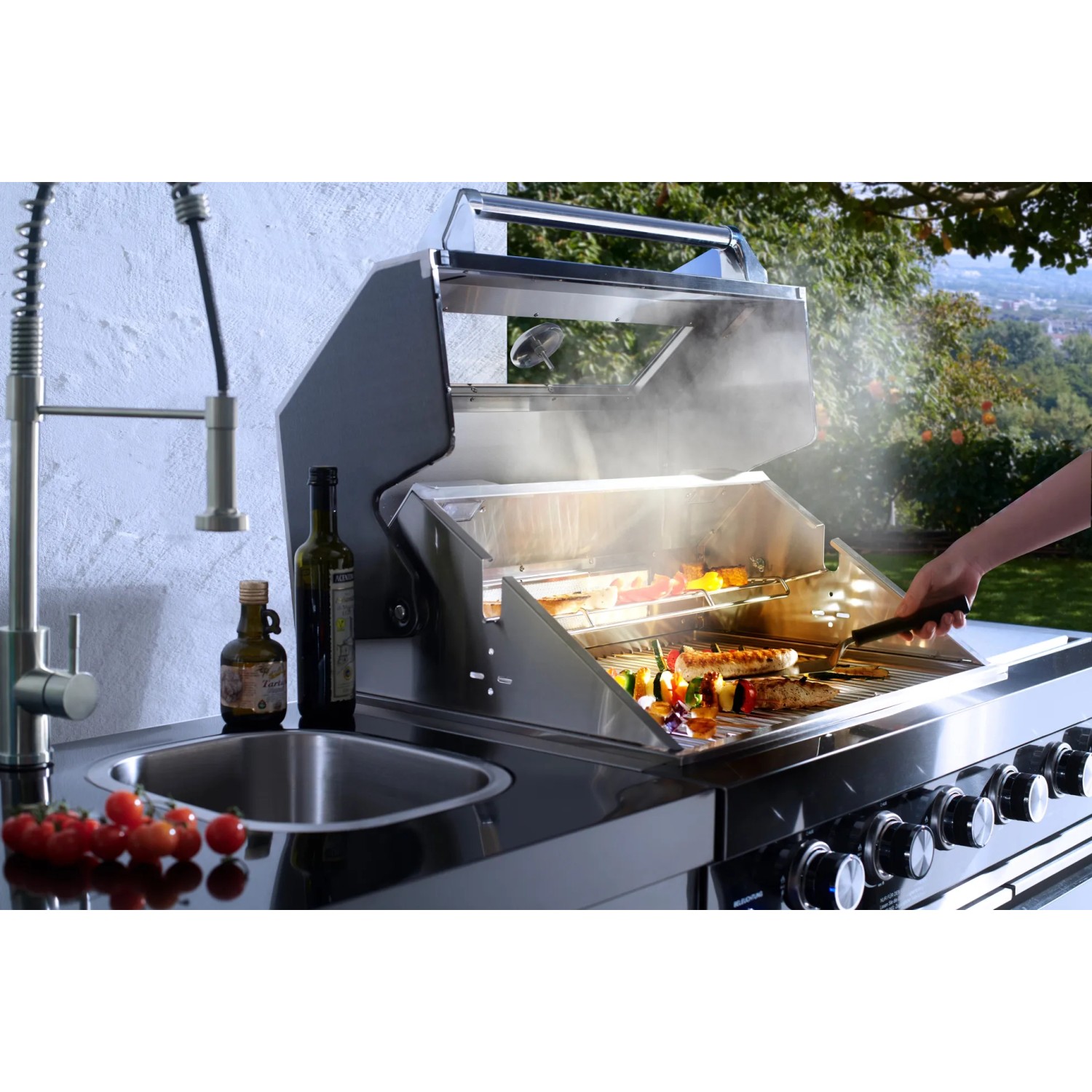 Buschbeck Outdoorküche Cambridge mit Grill, Spüle und Kühlschrank. Grillgut auf dem Rost.